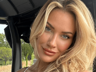 Paige Spiranac almost bursts out of a black top while smiling for the camera while sitting in a golf buggy